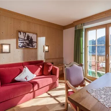 Ein gemütliches Wohnzimmer mit einem roten Sofa und einem Holzvertäfelungen. Durch die Fenster hat man einen schönen Blick auf die umliegende Landschaft.