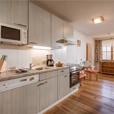 Eine moderne Küche mit hellen Schränken und Holzfußboden. Es gibt einen Herd, eine Mikrowelle und einen kleinen Essbereich.