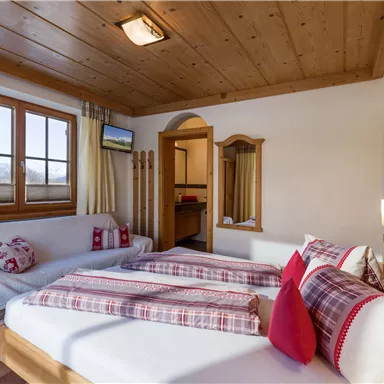 Ein gemütliches Schlafzimmer mit zwei Betten und Holzelementen. Der Raum hat große Fenster mit schöner Aussicht und ist in warmen Farben gestaltet.