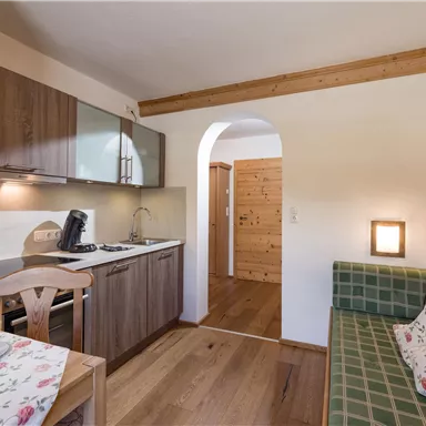 Eine moderne Küchenzeile mit Holzregalen und einem Esstisch. Der Raum hat einen gemütlichen Sitzbereich und warmes Holzdekor.