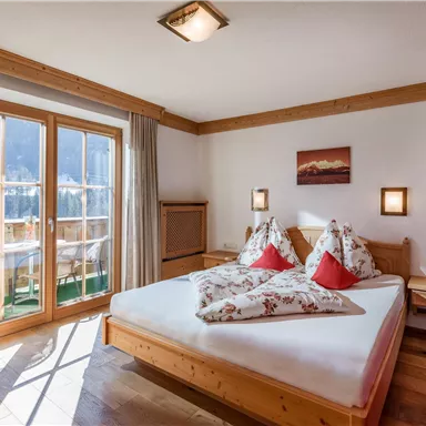 Ein gemütliches Schlafzimmer mit einem großen Bett und bunten Kissen. Es gibt Fenster mit Aussicht und warme Holzverkleidungen.