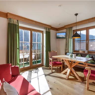 Ein gemütliches Wohnzimmer mit rotem Sofa und einem Holztisch. Große Fenster bieten Blick auf eine schöne Aussicht und viel Tageslicht.