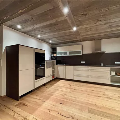 Modern kitchen with wooden ceiling and bright oak floorboards. The furniture is kept in neutral colors and offers plenty of storage space.