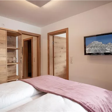 Ein modernes Schlafzimmer mit Holzschränken und einem Fernseher an der Wand. Die Bettwäsche ist gemütlich und in sanften Farben gehalten.