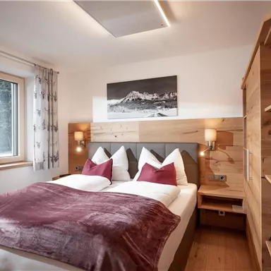 Ein gemütliches Schlafzimmer mit einem Doppelbett und eleganten Kissen. Holzregale und ein Fenster sorgen für eine helle Atmosphäre.