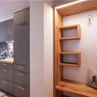 Eine moderne Küche mit grauen Schränken und einem Holzregal. Der Raum wirkt hell und einladend.