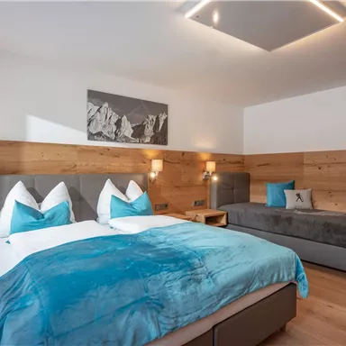 Ein modernes Hotelzimmer mit einem großen Doppelbett und einem Einzelbett. Die Wände sind aus Holz, und die Einrichtung ist in beruhigenden Blau- und Grautönen gehalten.