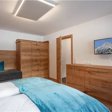 Ein modernes Schlafzimmer mit Holzmöbeln und einem großen Bett. An der Wand hängt ein Fernseher und es gibt einen gemütlichen Sitzbereich.