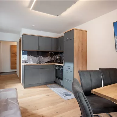 Eine moderne Küche mit Holzmöbeln und einem Esstisch. Der Raum ist hell und freundlich gestaltet.