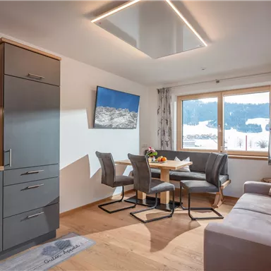 Eine moderne, helle Ferienwohnung mit offener Küche und Essbereich. Große Fenster bieten einen Blick auf die verschneite Landschaft.