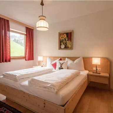 Ein gemütliches Schlafzimmer mit zwei Betten und Holzmöbeln. Große Fenster lassen viel Licht herein und die Wände sind in hellen Farben gehalten.