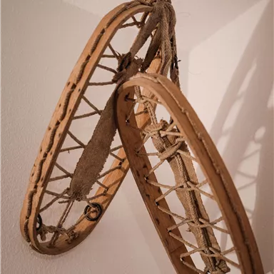 Zwei traditionelle Schneeschuhe hängen an der Wand. Sie sind aus Holz und Schnur gefertigt.
