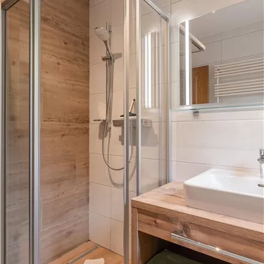 Ein modernes Badezimmer mit einer Duschkabine und einem Waschbecken. Die Wände sind hell gefliest, und das Design ist stilvoll und funktional.