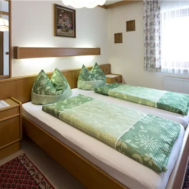 Ein gemütliches Schlafzimmer mit zwei Betten und grünen Kopfkissen. Der Raum hat Holzverkleidungen und große Fenster mit Licht.