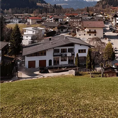 A picturesque village with a quiet residential area and mountains in the background. The houses are surrounded by meadows and trees.