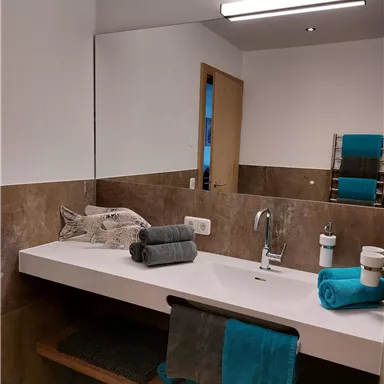 Ein modernes Badezimmer mit einem schlichten Waschbecken und stilvollen Handtüchern. Die Wände sind in neutralen Farbtönen gehalten, und es gibt ein gutes Licht durch die Deckenlampe.