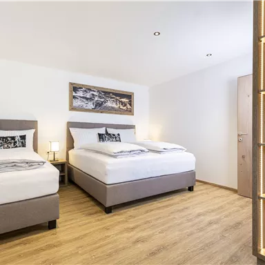 Ein gemütliches Zimmer mit zwei Einzelbetten und modernem Interieur. Lichtdurchflutet, mit einem schönen Holzregal und einer dekorativen Wandgestaltung.