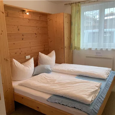 Ein gemütliches Schlafzimmer mit einem Doppelbett und Holzverkleidung. Durch die Fenster fällt natürliches Licht und die Dekoration ist einfach und einladend.