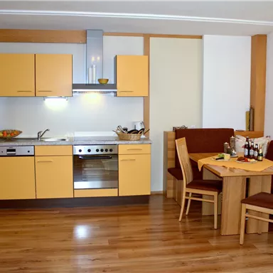 Eine moderne Küche mit gelben Schränken und Holzfußboden. Der Essbereich ist gemütlich mit einem Holztisch und Stühlen eingerichtet.