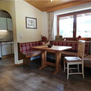 A cozy dining area with a wooden tray and an upholstered bench. The room is bright and cheerful, with a view of the window.
