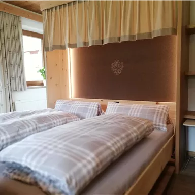 A cozy bedroom with two beds and checkered bedspreads. The wooden details and windows create a warm ambiance.