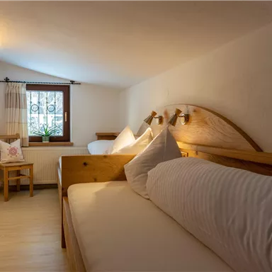 A cozy room with two beds and wooden furniture. Soft light falls through the window and there is a small plant on the windowsill.