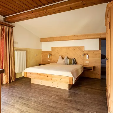 A cozy bedroom with a large bed and wooden interior. The windows let in a lot of light and offer a view outside.