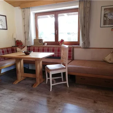 A cozy living space with a wooden table and benches. Large windows bring plenty of daylight into the room.