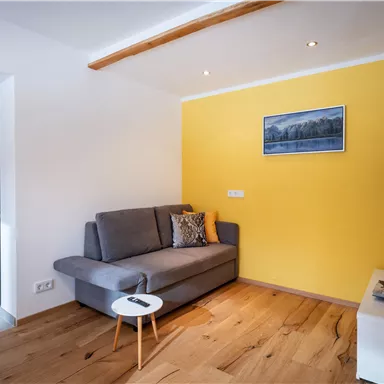 A modern living room with a gray sofa and yellow accents. A table and a TV complete the cozy decor.