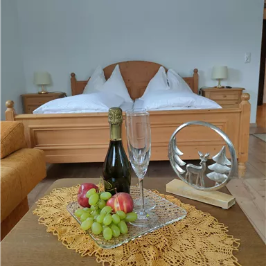 A cozy bedroom with a large bed and two nightstands. On the table, there are fruit, champagne, and a decorative object.