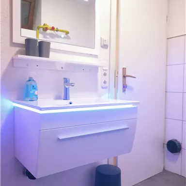A modern bathroom with a floating sink and an illuminated mirror. The walls are bright, and the fixtures look clean and contemporary.