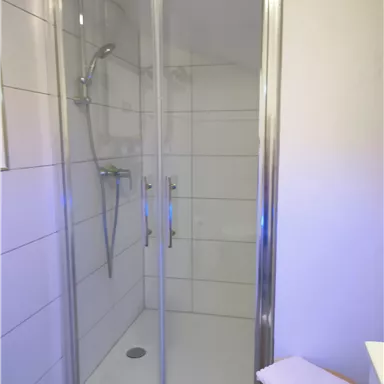 A modern shower with a glass wall and tiles. The space is bright and designed in a minimalist style.