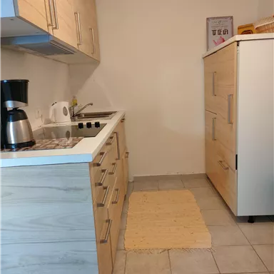 A modern kitchen with wooden cabinets and a countertop. There is a coffee machine, a stove, and a refrigerator.
