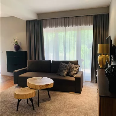 A modern living room with a cozy sofa and a wooden coffee table. Large windows provide plenty of daylight and an inviting atmosphere.