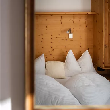 A cozy bedroom with wood paneling and white pillows. Part of the room is visible in the mirror.