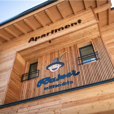 Ein modernes Apartmentgebäude aus Holz mit einem ausgeprägten Schild. Das Schild zeigt ein fröhliches Logo und den Schriftzug "Apartment".