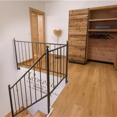 A modern hallway with a white handrail and wooden flooring. On the right side, there is an open wooden wardrobe.