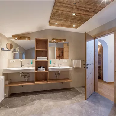 A modern bathroom with two sinks and wooden shelves. The warm lighting and bright colors create an inviting atmosphere.