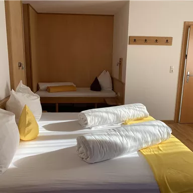 Ein modernes Schlafzimmer mit einem Doppelbett, weißen Bettwäsche und gelben Akzenten. Im Hintergrund gibt es eine gemütliche Sitzecke.