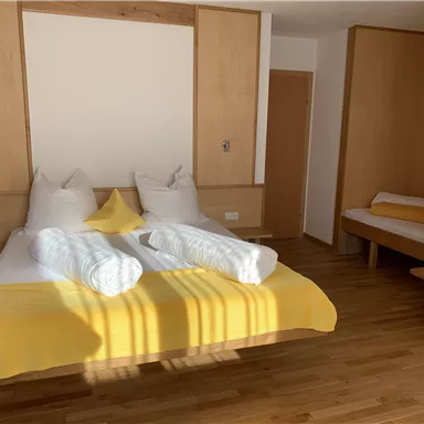 Ein helles Schlafzimmer mit einem großen Bett und zwei Kissen. Die Wände sind in warmen Holztönen gehalten, und es gibt einen einfachen Sitzbereich.