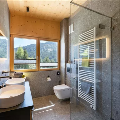 Ein modernes Badezimmer mit großen Fenstern und Blick auf die Berge. Es verfügt über zwei Waschbecken und eine geflieste Dusche.