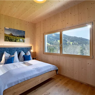 Ein gemütliches Schlafzimmer mit Holzverkleidung und großen Fenstern. Man hat einen schönen Blick auf die Berge.
