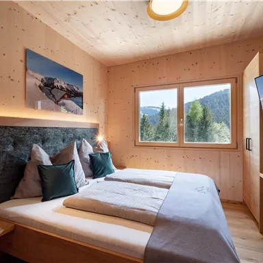 Ein modernes Schlafzimmer mit hellem Holzdekor und großen Fenstern. Der Raum ist gemütlich eingerichtet und bietet einen Blick auf die umliegenden Berge.