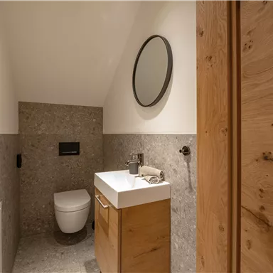 Ein modernes Badezimmer mit einem hängenden WC und einer eleganten Waschtischkombination aus Holz. Der Raum hat eine helle und minimalistische Gestaltung mit einem runden Spiegel.