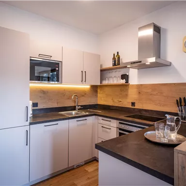 A modern kitchen with bright cabinets and wood accents. It features a sink, a stove, and dishes on the countertop.