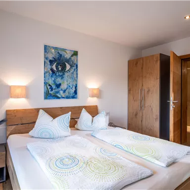 A modern bedroom with a double bed and two nightstands. A painting hangs on the wall, and there is access to the bathroom.