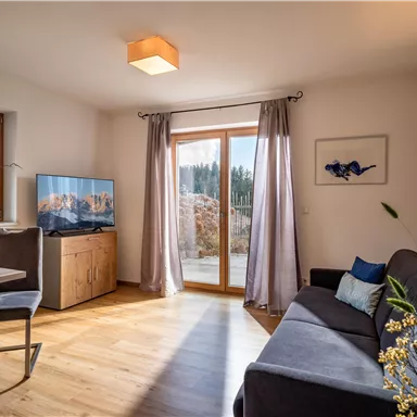 A modern living room with a cozy couch and a table. Large windows let in plenty of light and offer a view of nature.