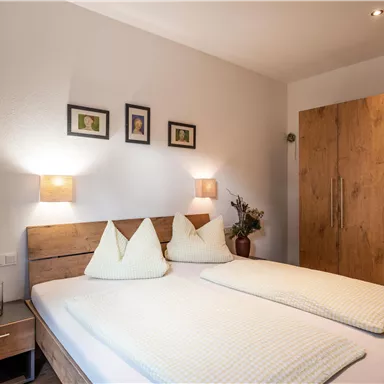 A cozy bedroom with a double bed and soft lighting. Some pictures hang on the wall, and a wardrobe stands in the room.