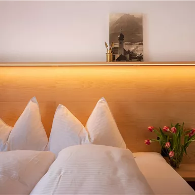 A cozy bedroom with three pillows and stylish wood paneling. Fresh tulips and a decorative picture are on the nightstand.