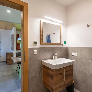 A modern bathroom with a wooden vanity and a large mirror. Towels hang on the walls and the space feels bright and inviting.